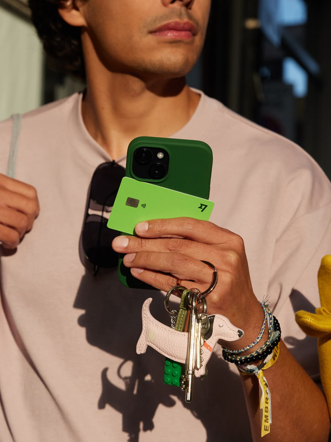 A man is walking down a shopping street. He holds his phone, keys, sunglasses and a Wise Multi-Currency Card in his hand.