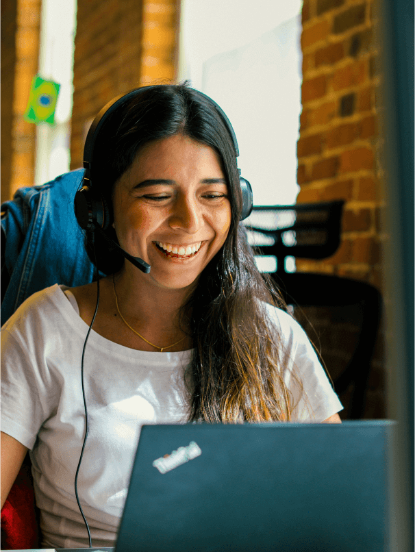 Smiling woman with a headset working on a laptop.