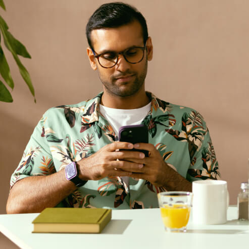 一个男人坐在咖啡馆的一张桌子旁，使用智能手机 App 查看他的 Wise 账号。